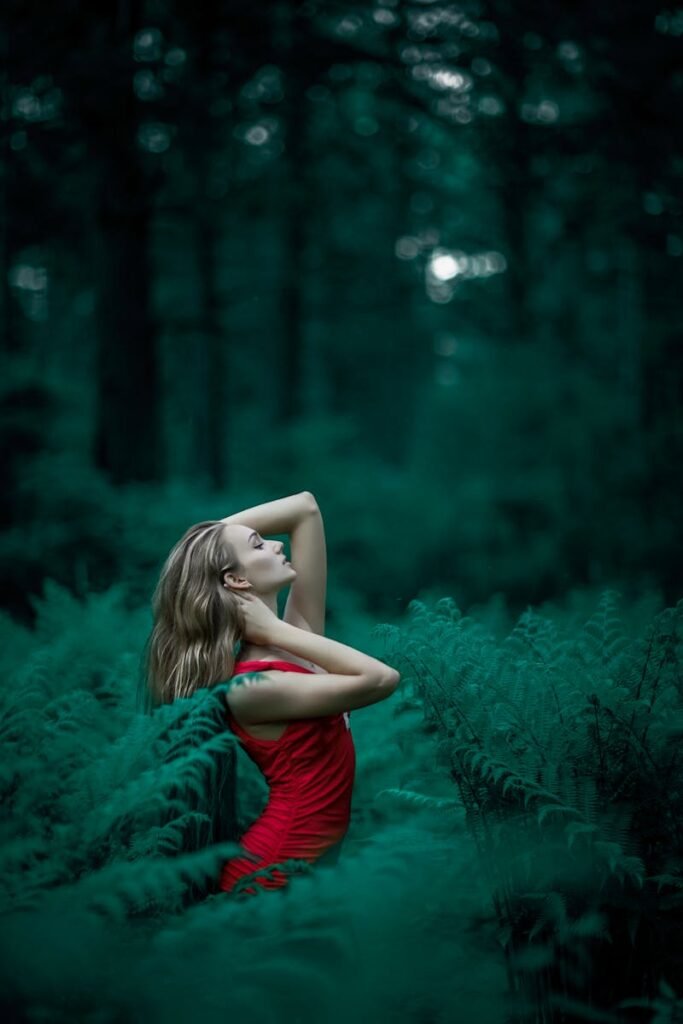 Clinica Estetica Dr Garcia Valdemoro A woman poses in a vibrant red dress amidst lush green ferns in an enchanting forest setting.